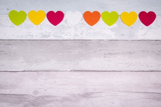 Colorful felt hearts on a background of old wooden planks resembling an old parquet floor. Concept of valentine's day and love in general.