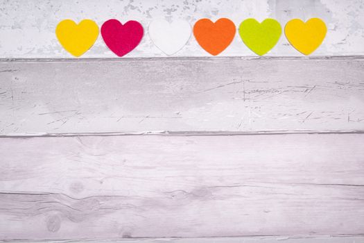 Colorful felt hearts on a background of old wooden planks resembling an old parquet floor. Concept of valentine's day and love in general.