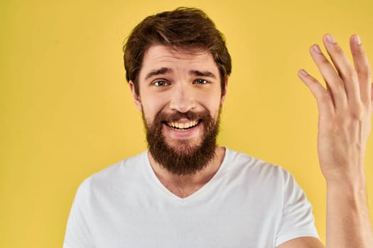 A man in a white t-shirt gestures with his hands lifestyle cropped view yellow background more fun. High quality photo