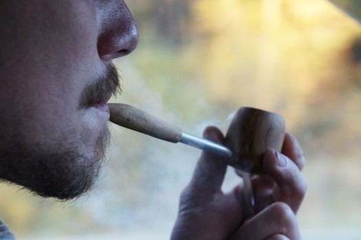 young man smoking a pipe, side view close up