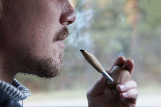 young man smoking a pipe, side view close up