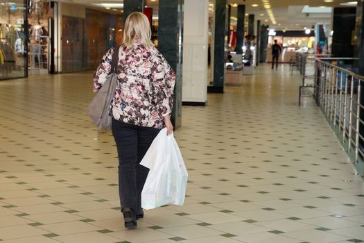 woman with purchases walking through the mall, back view.