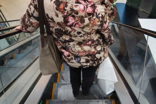 woman with shopping rides on the escalator down in the mall, back view