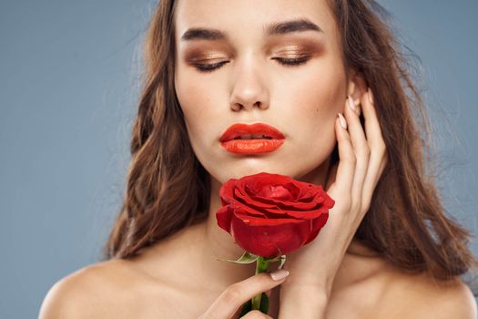 Woman portrait with red rose near the face on gray background and makeup curly hair. High quality photo