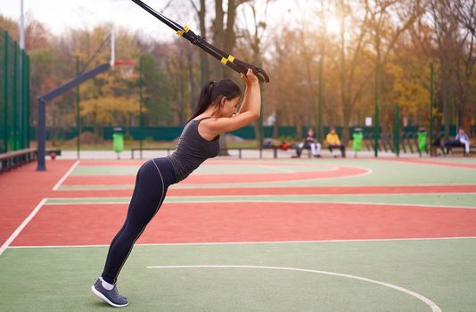 Girl athlete training using trx sportground Mixed race young adult woman workout suspension system Healthy lifestyle Stretching outdoors playground. Make your body machine