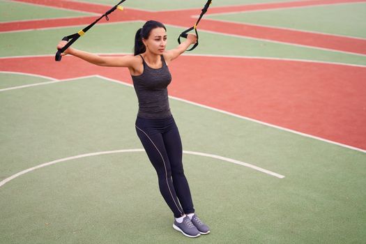 Girl athlete training using trx sportground Mixed race young adult woman workout suspension system Healthy lifestyle Stretching outdoors playground. Make your body machine