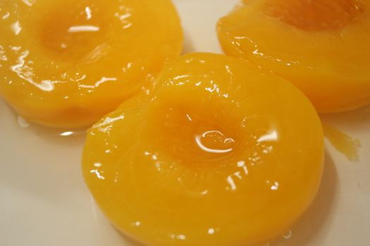 Closeup high angle view with selective focus of yellow peaches slices. Canned peaches halves sprinkled with syrup in white plate.