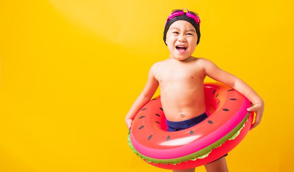 Summer vacation concept, Portrait Asian happy cute little child boy wear goggles and swimsuit hold watermelon inflatable ring, Kid having fun on summer vacation, studio shot isolated yellow background