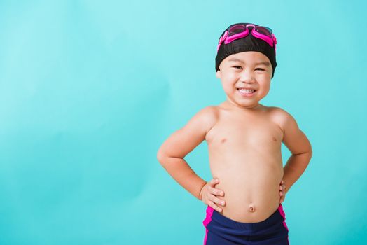 Summer vacation concept, Closeup portrait Asian happy cute little child boy wearing goggles and swimsuit, Kid having fun with in summer vacation looking camera, studio shot isolated blue background