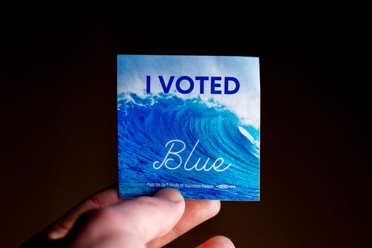 November 3, 2020 - Elkins Park, Pennsylvania: An Election Day Sticker Held by a Hand That Says I Voted Blue With a Wave in the Background on Black