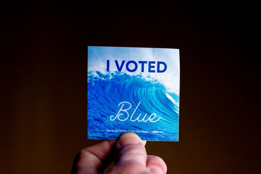 November 3, 2020 - Elkins Park, Pennsylvania: An Election Day Sticker Held by a Hand That Says I Voted Blue With a Wave in the Background on Black