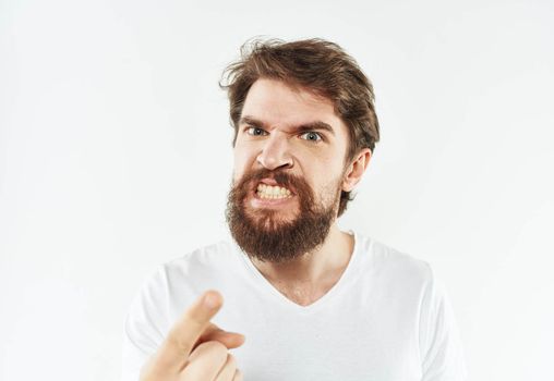A bearded man in a white T-shirt gestures with his hands on a light background. High quality photo