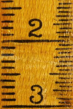 Numbers two and three on a yellow  wooden ruler , black lines along the edges ,the ruler is worn out