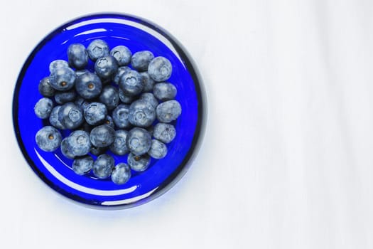 Beautiful blueberries in a blue glass bowl ,the bowl is on a white cloth 