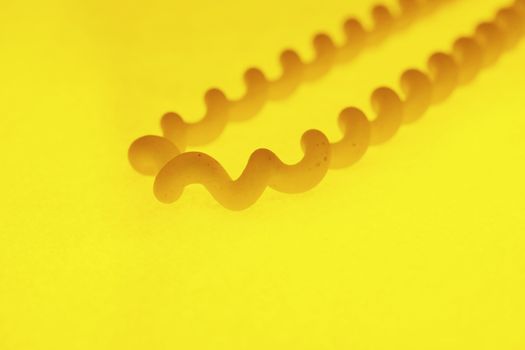 Italian pasta called fusilli , long thin corkscrew shaped pasta on a yellow background, macro photography