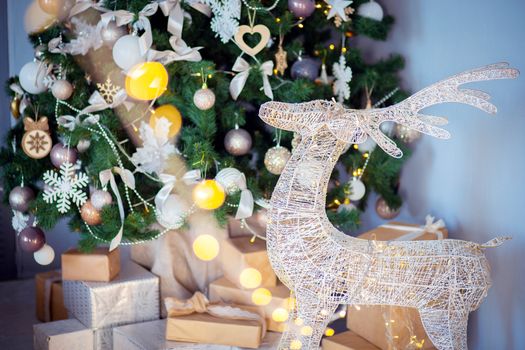 A festive decorative deer stands in the room against the background of a Christmas tree and a mountain of gifts. Gifts for the new year under the tree. Holiday atmosphere