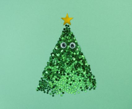 Christmas tree shape from confetti stars with eyes on green paper.