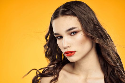 Beautiful brunette naked shoulders bright makeup red lips hairstyle close-up yellow background. High quality photo