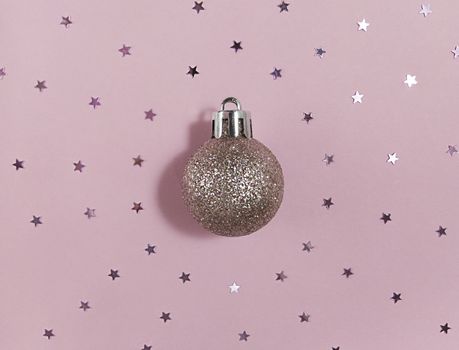 Glitter Christmas tree ball and confetti stars on pink paper. Festive flat lay.