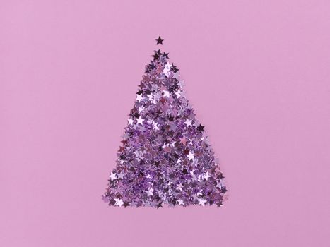 Christmas tree shape from confetti stars on pink paper. Festive monochrome flat lay.