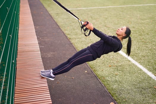 Girl athlete training using trx sportground Mixed race young adult woman workout suspension system Healthy lifestyle Stretching outdoors playground. Make your body machine