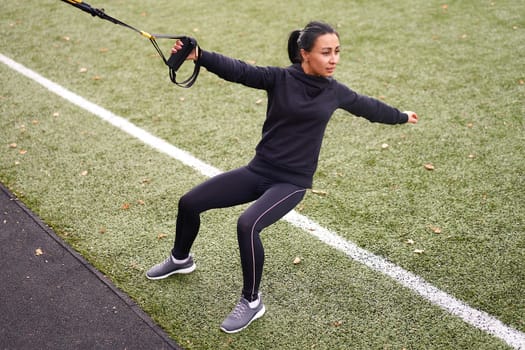 Girl athlete training using trx sportground Mixed race young adult woman workout suspension system Healthy lifestyle Stretching outdoors playground. Make your body machine