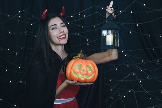 Caucasian woman dressed in Halloween witch costume. Attractive young women holding a carved pumpkin and a magic lamp. Have fun at a party Halloween Celebration. Fantasy, magic, and darkness concept.
