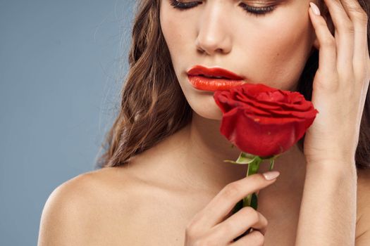 Woman portrait with red rose near the face on gray background and makeup curly hair. High quality photo