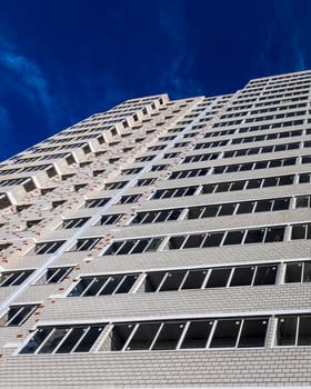 Fragment of a white brick residential building with balconies against a clear sky.