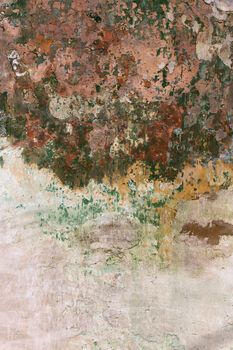 Old obsolete wall with layers of green paint, brick red and white plaster peeling