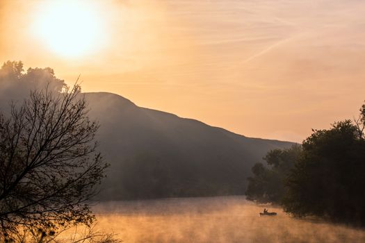 Silhouette of a fisherman in a boat on a foggy river in the morning