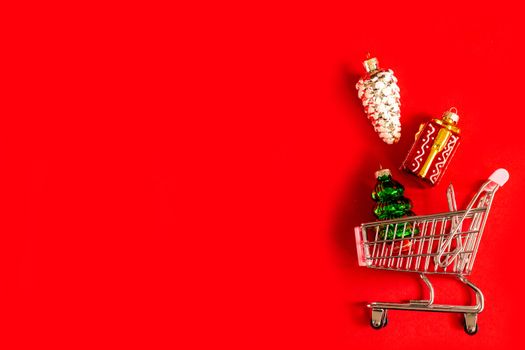 A full shopping basket of different glass and glossy Christmas tree toys on a red background. Christmas toys are spilled out of the store's basket. online shopping, Christmas shopping, black Friday.