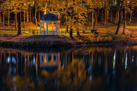 Night in autumn park with pond and white rotunda