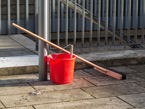 Broom and red water bucket on paving stones