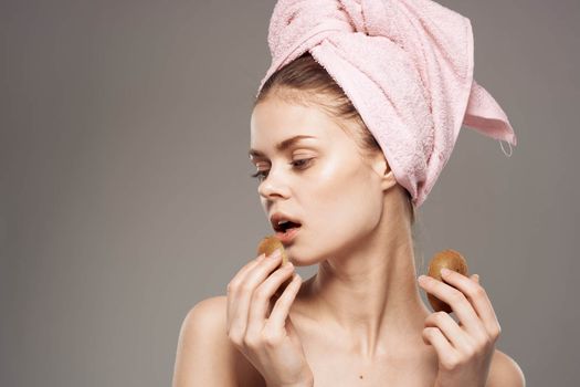 beautiful woman with pink towel on her head naked shoulders kiwi in hands health skin care. High quality photo