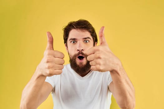 Bearded man emotions fun gesture with hands white t-shirt close-up yellow background. High quality photo