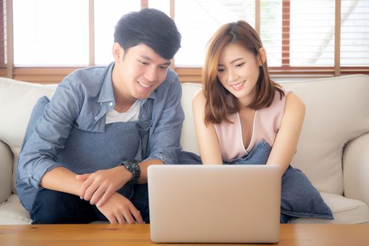 Asian young couple using laptop computer think and searching internet together, man and woman casual smiling work at home with happy and relax, communication and business concept.