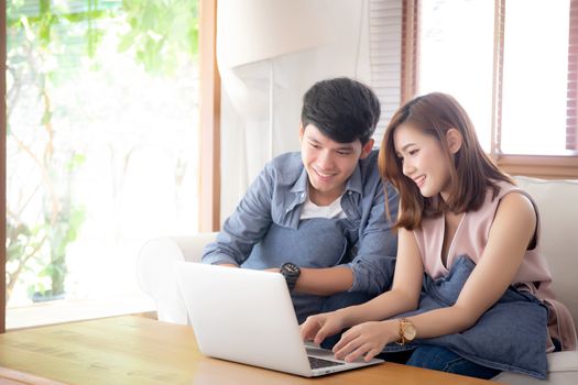 Asian young couple using laptop computer think and searching internet together, man and woman casual smiling work at home with happy and relax, communication and business concept.