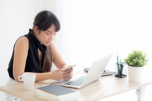 Beautiful young asian woman working laptop computer online to internet and texting message on smart mobile phone, freelance using notebook, business and communication concept.