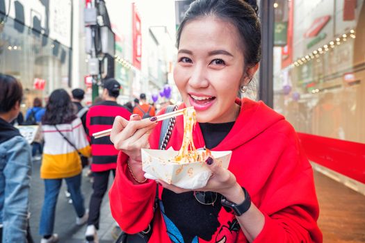 Young woman eating Roasted lobster with cheese at Myeong-dong street food in Seoul, South Korea
