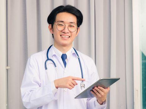 Portrait closeup of Happy Asian young doctor handsome man smiling in uniform and stethoscope neck strap holding and point smart digital tablet and looking to the camera, healthcare medicine concept