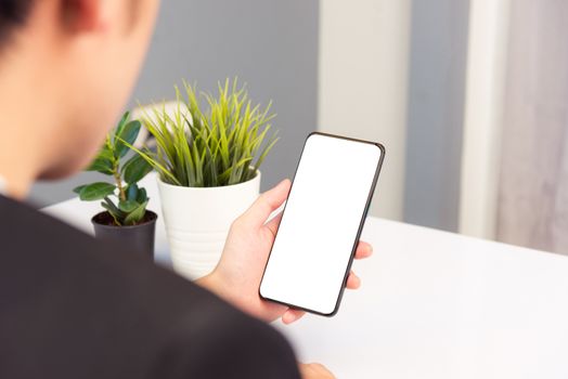 Work from home, Back view of Asian young businessman smile wearing suit video conference call or facetime by smart digital mobile phone blank screen listen carefully to your co-workers on desk