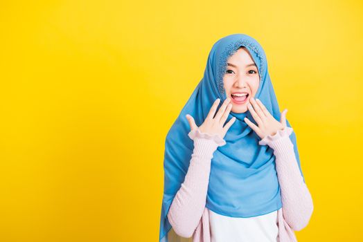 Asian Muslim Arab, Portrait of happy beautiful young woman Islam religious wear veil hijab funny smile she shocking open mouth touching her cheeks with hands isolated yellow background