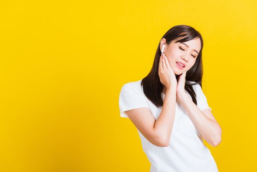 Portrait Asian of a happy beautiful young woman wear wireless earphone listening to music from smartphone having fun and dancing to sounds of favorite music studio shot isolated on yellow background