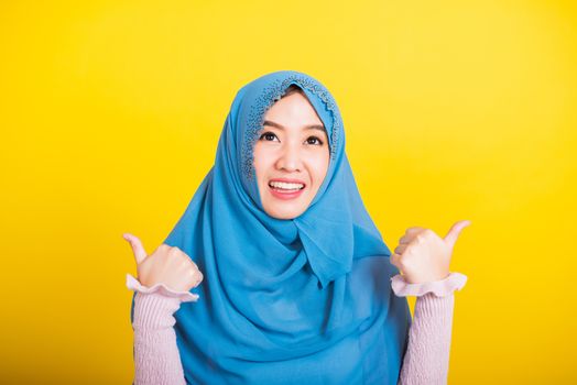 Asian Muslim Arab, Portrait of happy beautiful young woman Islam religious wear veil hijab funny smile she made finger thumbs up, Ok sign to agree, studio shot isolated on yellow background