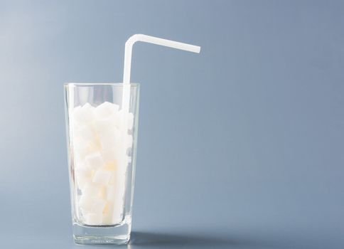 A glass full of white sugar cube sweet food ingredient, studio shot isolated on a gray background, health high blood risk of diabetes and calorie intake concept and unhealthy drink