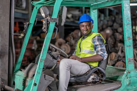 Portrait of African American factory man with smiling sit on forklift during work in workplace area of automotive or mechanic part. Concept of happiness during work in mechanical industrial business.