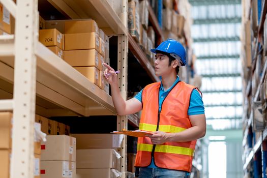 Warehouse man or factory worker with blue hard hat and uniform stand between shelves and check package in workplace. Concept of good management and happiness of staff during work industrial business.