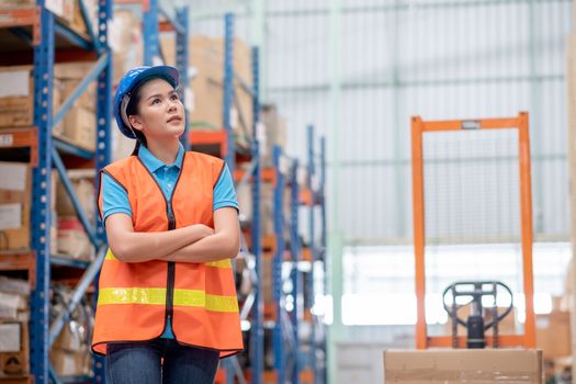 Warehouse woman or factory worker with blue hard hat and uniform stand in front of hydraulic cart in workplace. Concept of good management and happiness of staff during work in business.