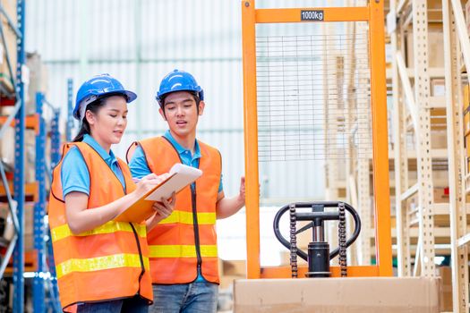 Warehouse man and woman or factory workers discuss together about checking stock of products and stand with hand stacker or hydraulic cart in workplace area for delivery industrial business.